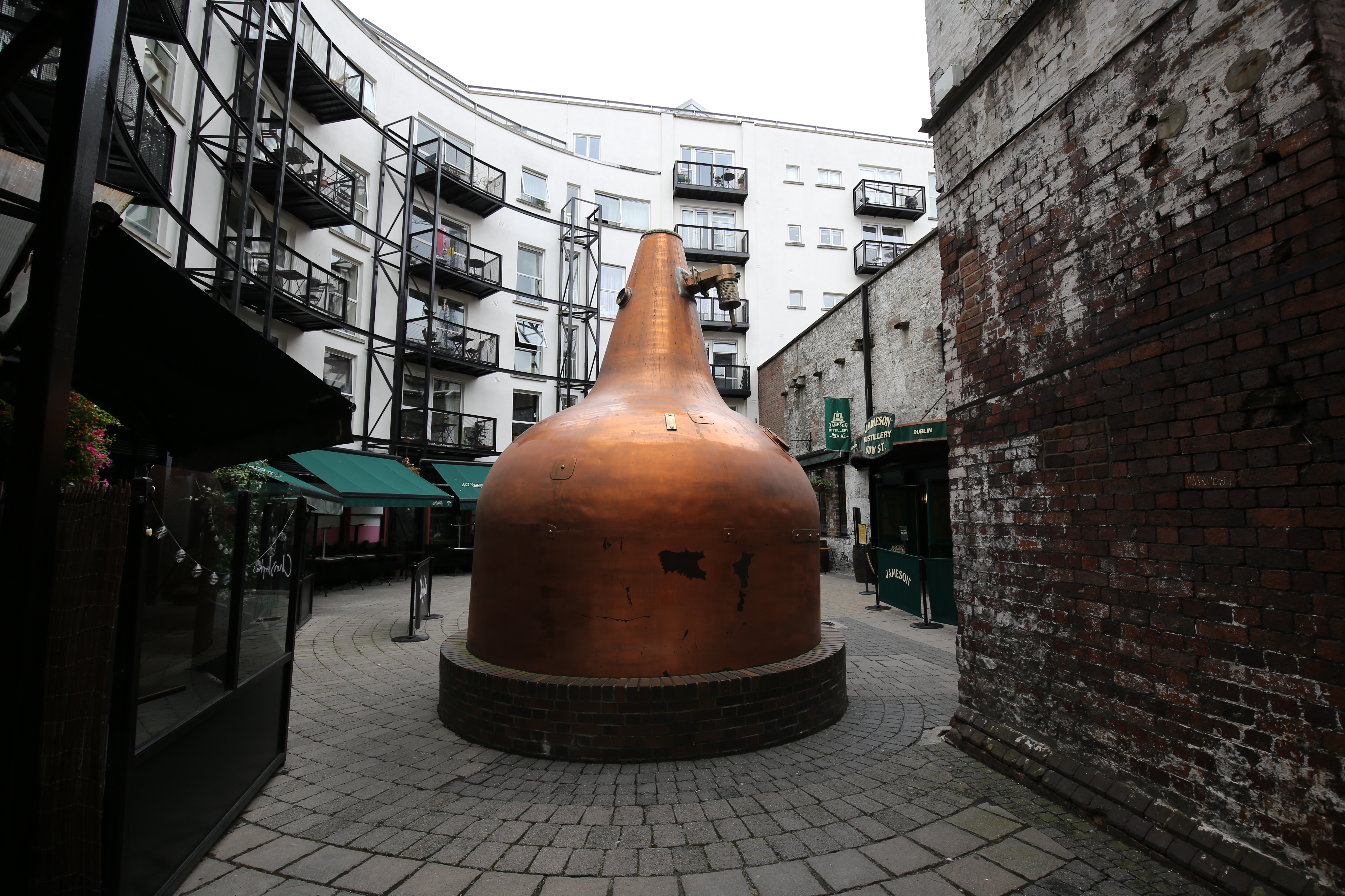 Photograph of a large copper distillery kettle in a cobbled courtyard.