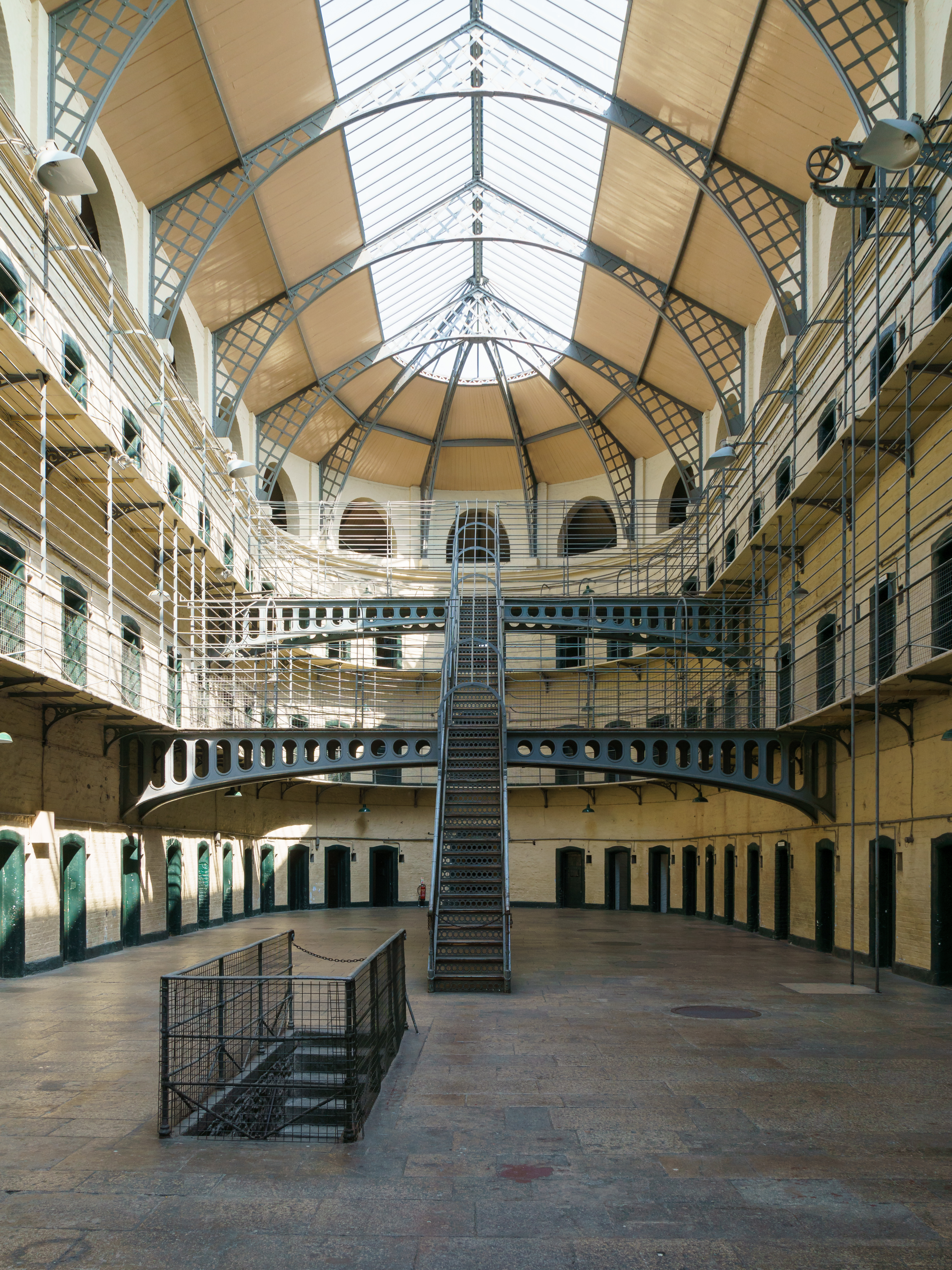 Photograph from the inside of Kilmainham Gaol, showing three stories of cells with green doors, naturally lit through the giant skylight.