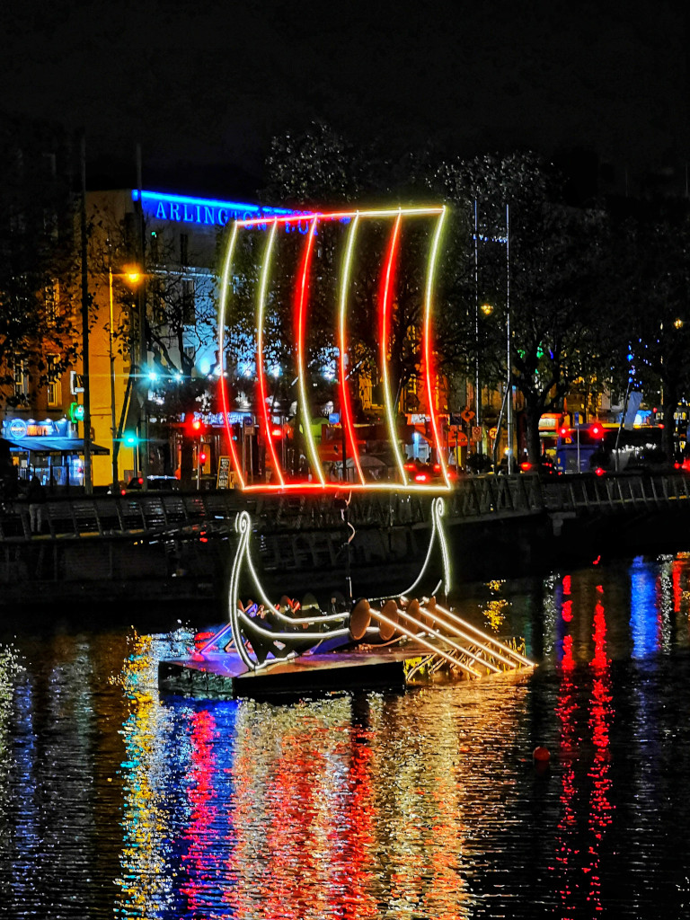 A full-size viking light ship made from LED strips lights up the river it is floating on.