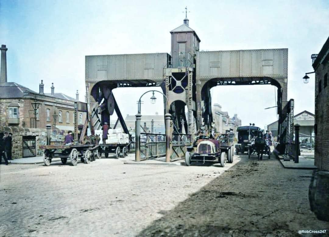 An old movable Bridge, made of metal and with a central control box. On the left are old red-brick offices. 