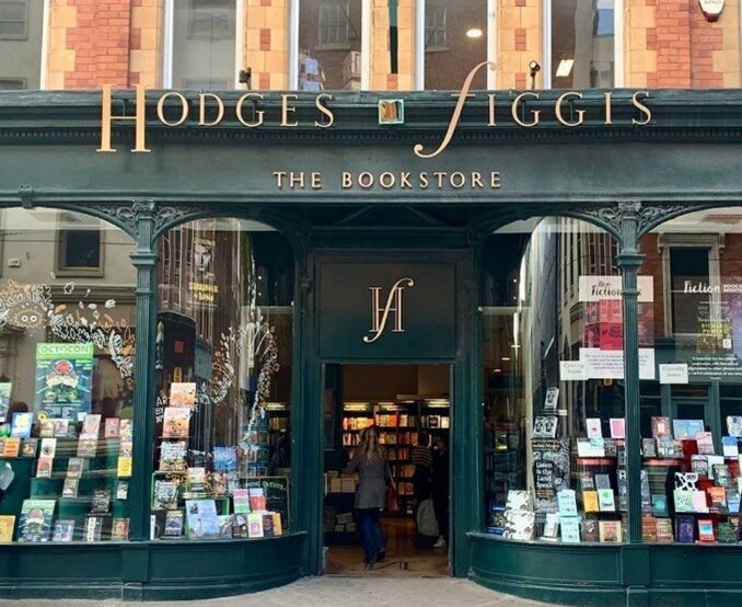 The front of the modern Hodges Figgis bookshop. It shows a red-brick upper story and a ground floor with curved windows on either side of a central door. The bookshop has dark green frontage with the sign Hodges Figgis over the door.