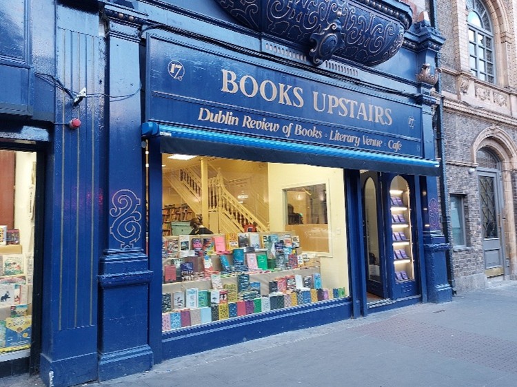 A bookshop with 'Books upstairs' in the sign above the wondow and a large number of books displayed in the window.