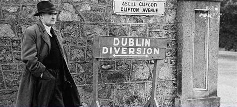 A black-and-white photo of a man in early 20th century clothing, standing beside a sign that says 'Dublin Diversion'.
