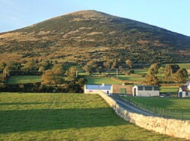 A hill in the Irish Countryside. A small farmhouse and barn is visible in the foreground.